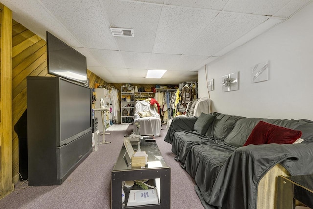 carpeted living room featuring a drop ceiling, visible vents, and wooden walls