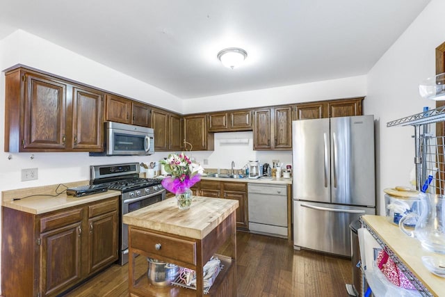 kitchen with dark wood finished floors, stainless steel appliances, dark brown cabinets, light countertops, and a sink