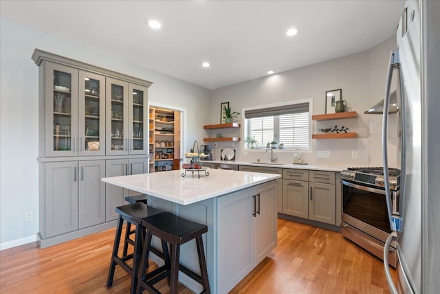 kitchen with light wood-style flooring, gray cabinetry, light countertops, appliances with stainless steel finishes, and open shelves