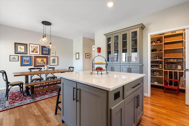 kitchen featuring a center island, pendant lighting, light wood-style flooring, gray cabinetry, and glass insert cabinets