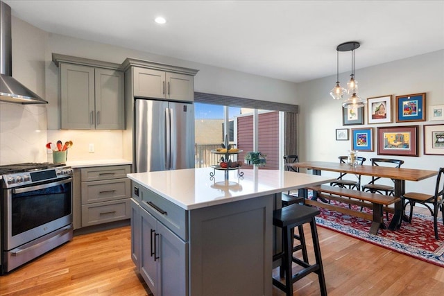 kitchen with light wood finished floors, appliances with stainless steel finishes, wall chimney range hood, and gray cabinetry