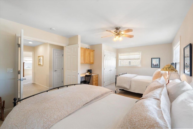 bedroom featuring a closet, built in study area, ceiling fan, light carpet, and baseboards