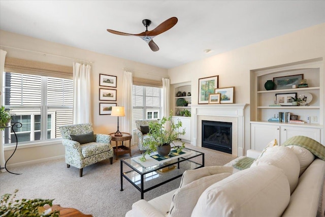 carpeted living room with baseboards, built in features, a ceiling fan, and a glass covered fireplace