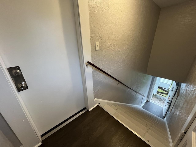 stairway with a textured wall, baseboards, and wood finished floors