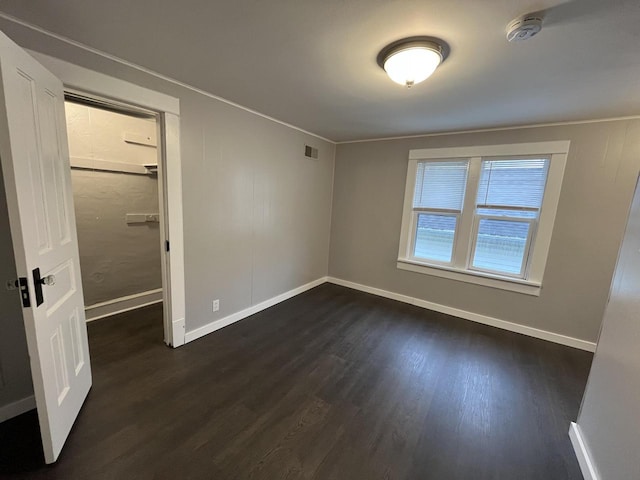 unfurnished bedroom with a walk in closet, visible vents, baseboards, and dark wood finished floors