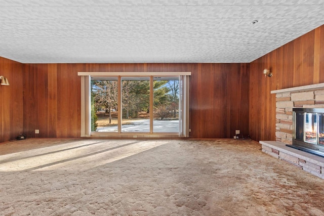 unfurnished living room with a fireplace, carpet flooring, and wooden walls