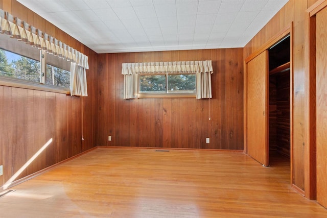 unfurnished room with light wood finished floors, wooden walls, and a wealth of natural light