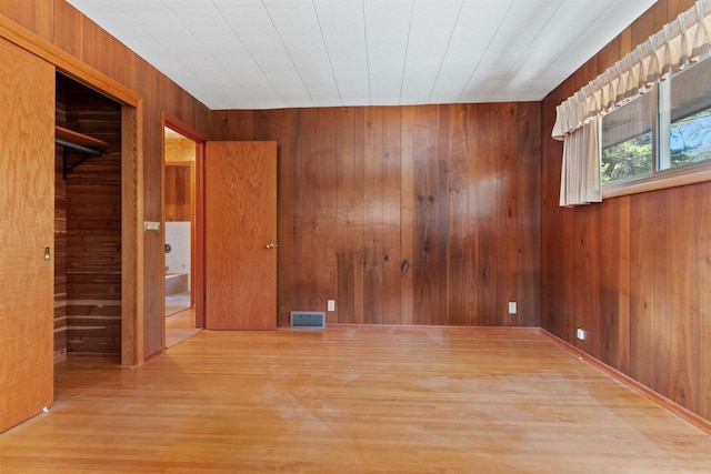 empty room with wooden walls, visible vents, and wood finished floors