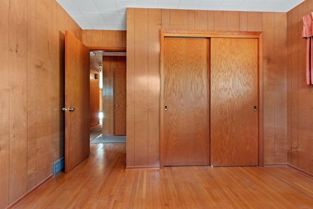 unfurnished bedroom with a closet, wood finished floors, and wooden walls