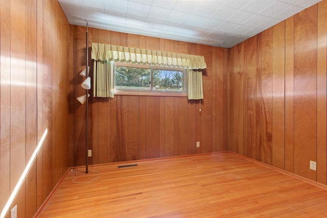 unfurnished room with visible vents, wood walls, and wood finished floors