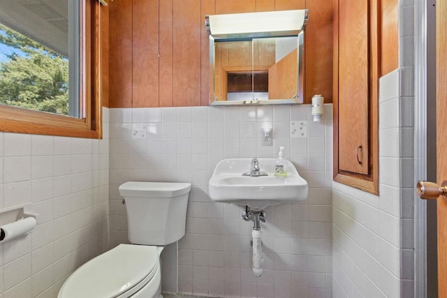 bathroom featuring toilet, tile walls, and a sink