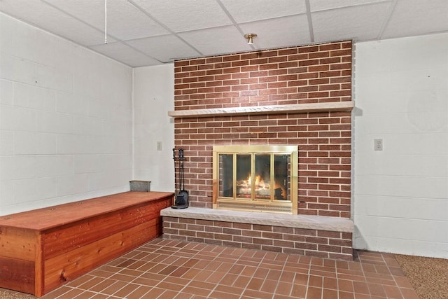 interior details with concrete block wall, a fireplace, and a drop ceiling