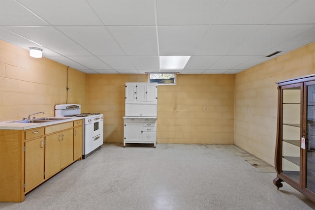 interior space with a paneled ceiling, a sink, white range with gas cooktop, light countertops, and concrete block wall