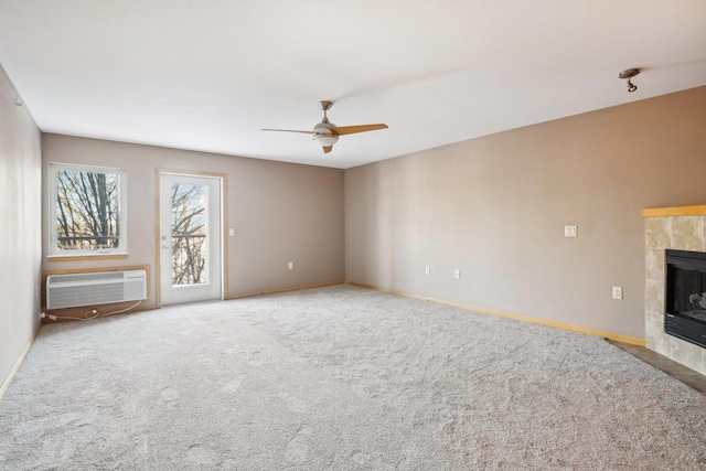 unfurnished living room featuring a tile fireplace, light colored carpet, a ceiling fan, baseboards, and an AC wall unit