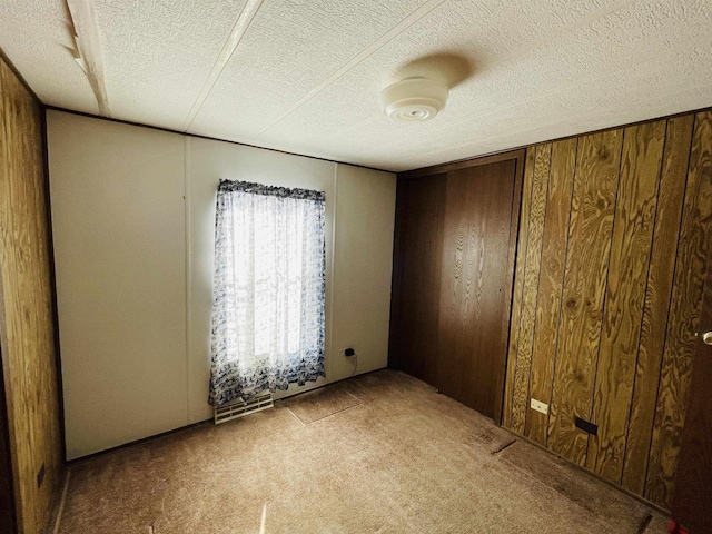 empty room with light carpet, wooden walls, and a textured ceiling