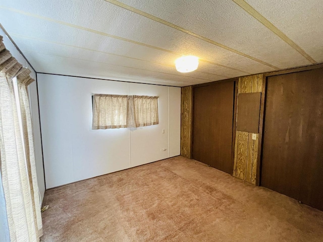 unfurnished bedroom with a textured ceiling, multiple windows, wood walls, and light colored carpet