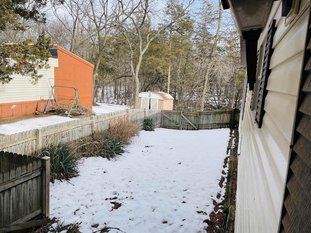 yard layered in snow featuring a fenced backyard and a storage shed