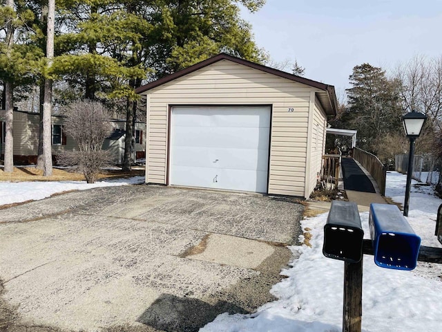 snow covered garage with driveway and a detached garage