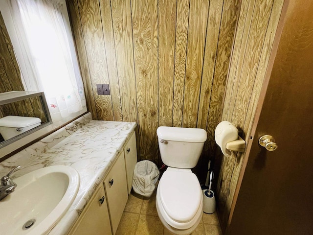 bathroom with toilet, wood walls, tile patterned flooring, and vanity