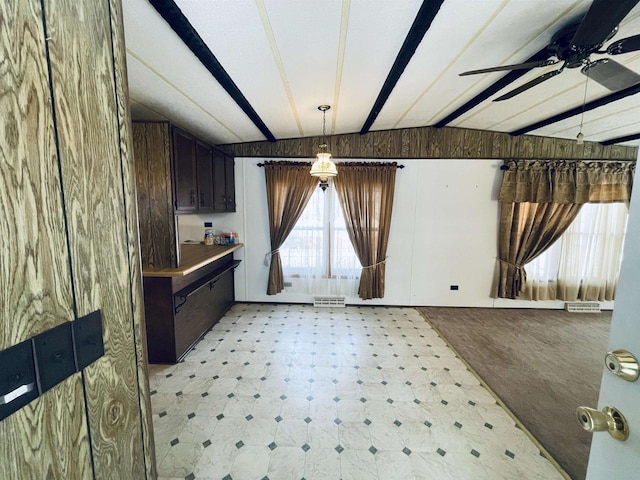 interior space with vaulted ceiling with beams, dark brown cabinets, light floors, and wooden walls