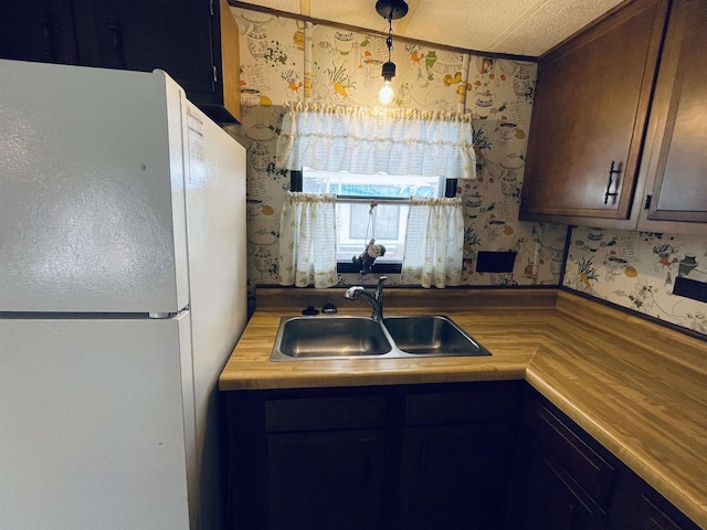 kitchen featuring wallpapered walls, decorative light fixtures, a sink, and freestanding refrigerator