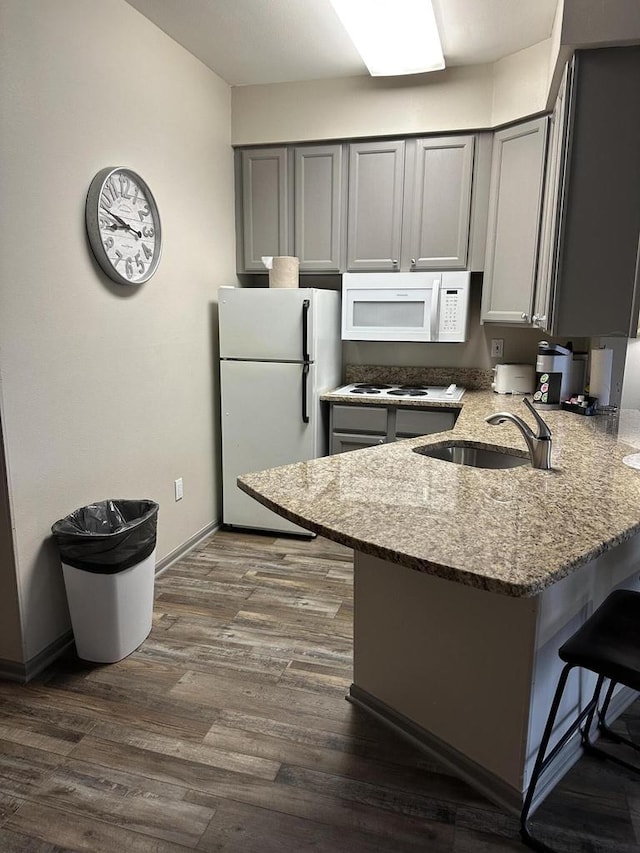 kitchen with gray cabinets, a sink, white appliances, a peninsula, and light stone countertops