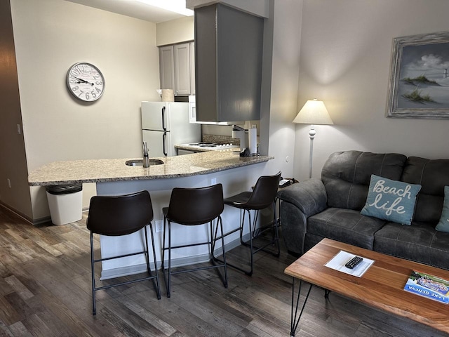 kitchen with a kitchen bar, dark wood-style flooring, freestanding refrigerator, and a sink