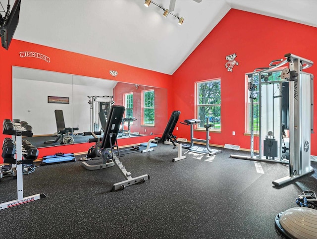 exercise room featuring high vaulted ceiling, baseboards, and visible vents