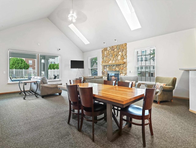 carpeted dining room with a skylight, baseboards, high vaulted ceiling, and a stone fireplace