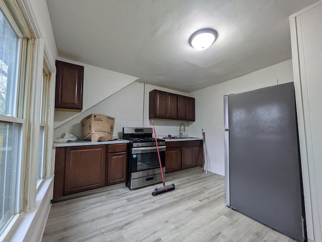 kitchen with light countertops, light wood-style flooring, appliances with stainless steel finishes, a sink, and dark brown cabinetry