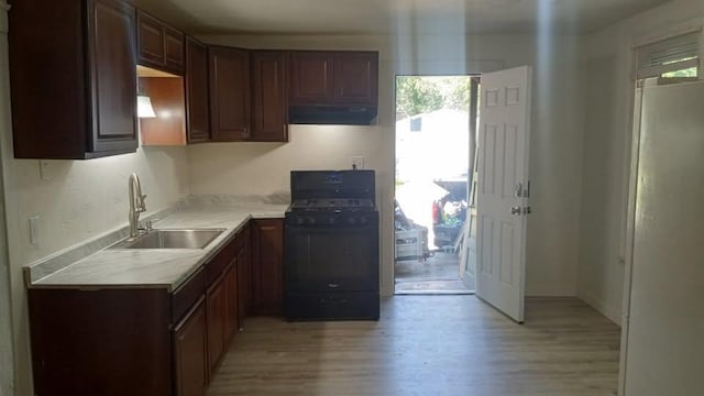 kitchen featuring black range with gas cooktop, light wood-style flooring, light countertops, under cabinet range hood, and a sink