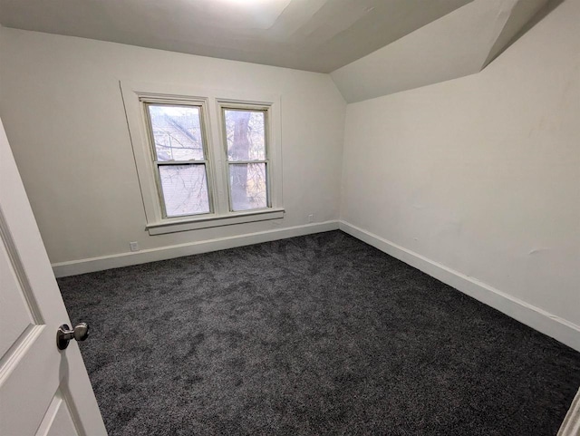 empty room featuring baseboards, vaulted ceiling, and dark colored carpet