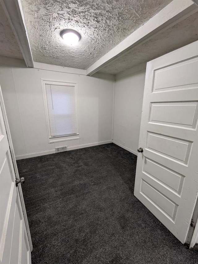 interior space featuring visible vents, dark carpet, a textured ceiling, and baseboards