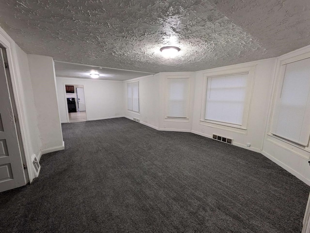 unfurnished room featuring baseboards, visible vents, dark colored carpet, and a textured ceiling