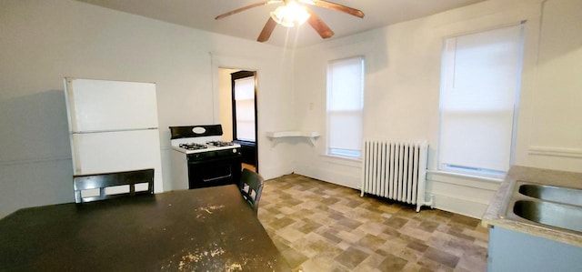 kitchen featuring a ceiling fan, radiator heating unit, freestanding refrigerator, a sink, and gas stove