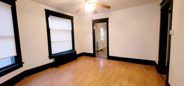 unfurnished room with radiator, ceiling fan, light wood-style flooring, and baseboards