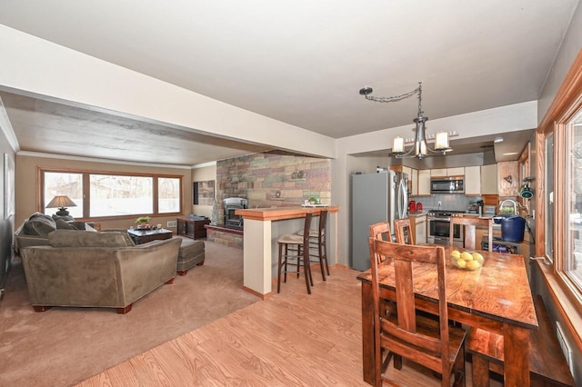 dining area featuring light wood-type flooring, an inviting chandelier, ornamental molding, and a stone fireplace