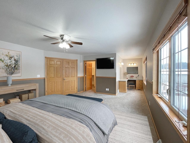 bedroom with a textured ceiling, connected bathroom, light colored carpet, a ceiling fan, and baseboards