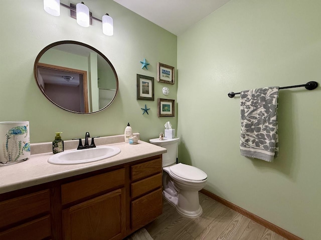 half bathroom with baseboards, vanity, toilet, and wood finished floors