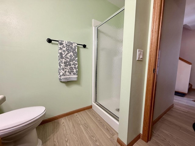 bathroom featuring wood finished floors, a shower stall, toilet, and baseboards