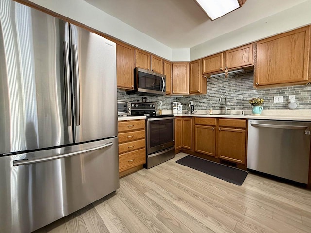 kitchen with brown cabinetry, stainless steel appliances, a sink, and light countertops