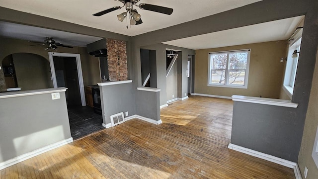 spare room with ceiling fan, hardwood / wood-style flooring, visible vents, baseboards, and a wood stove