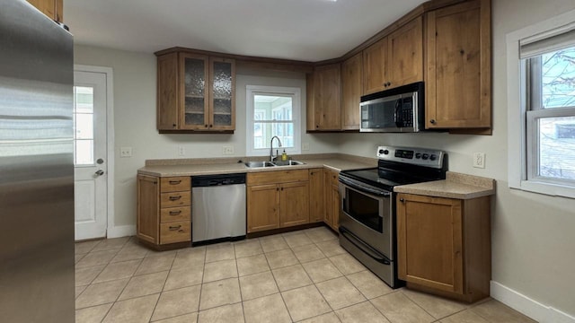 kitchen with glass insert cabinets, appliances with stainless steel finishes, light countertops, a healthy amount of sunlight, and a sink