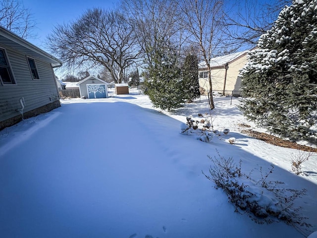 yard covered in snow featuring a storage shed, an outdoor structure, and fence