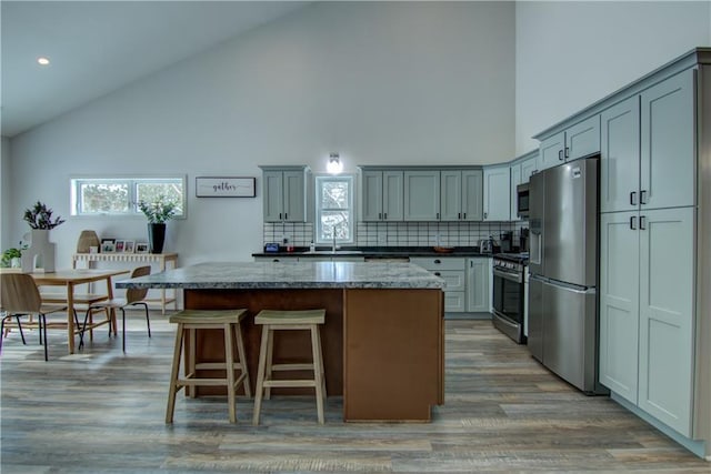 kitchen with dark stone countertops, a center island, stainless steel appliances, light wood-type flooring, and backsplash