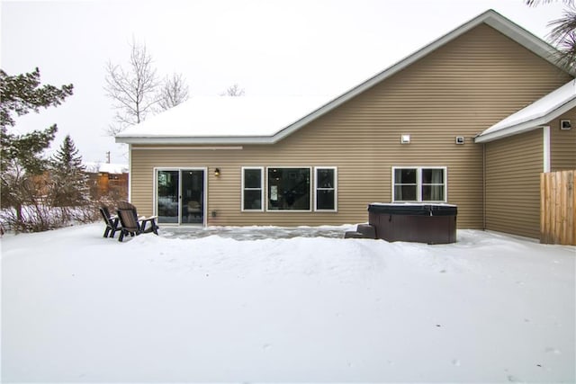 snow covered rear of property with fence and a hot tub