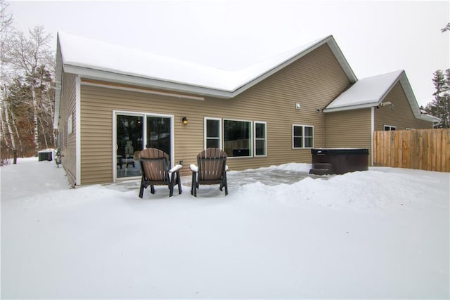 snow covered property featuring a hot tub, fence, and central AC