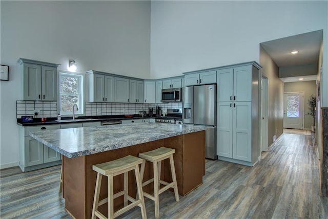 kitchen with stainless steel appliances, wood finished floors, a sink, backsplash, and a center island