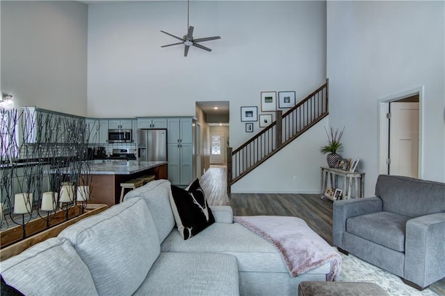 living room with dark wood-type flooring, ceiling fan, a towering ceiling, and stairs