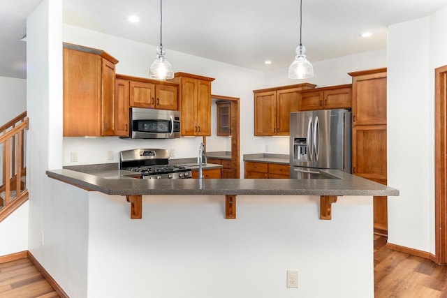 kitchen with appliances with stainless steel finishes, light wood-type flooring, brown cabinetry, and a peninsula